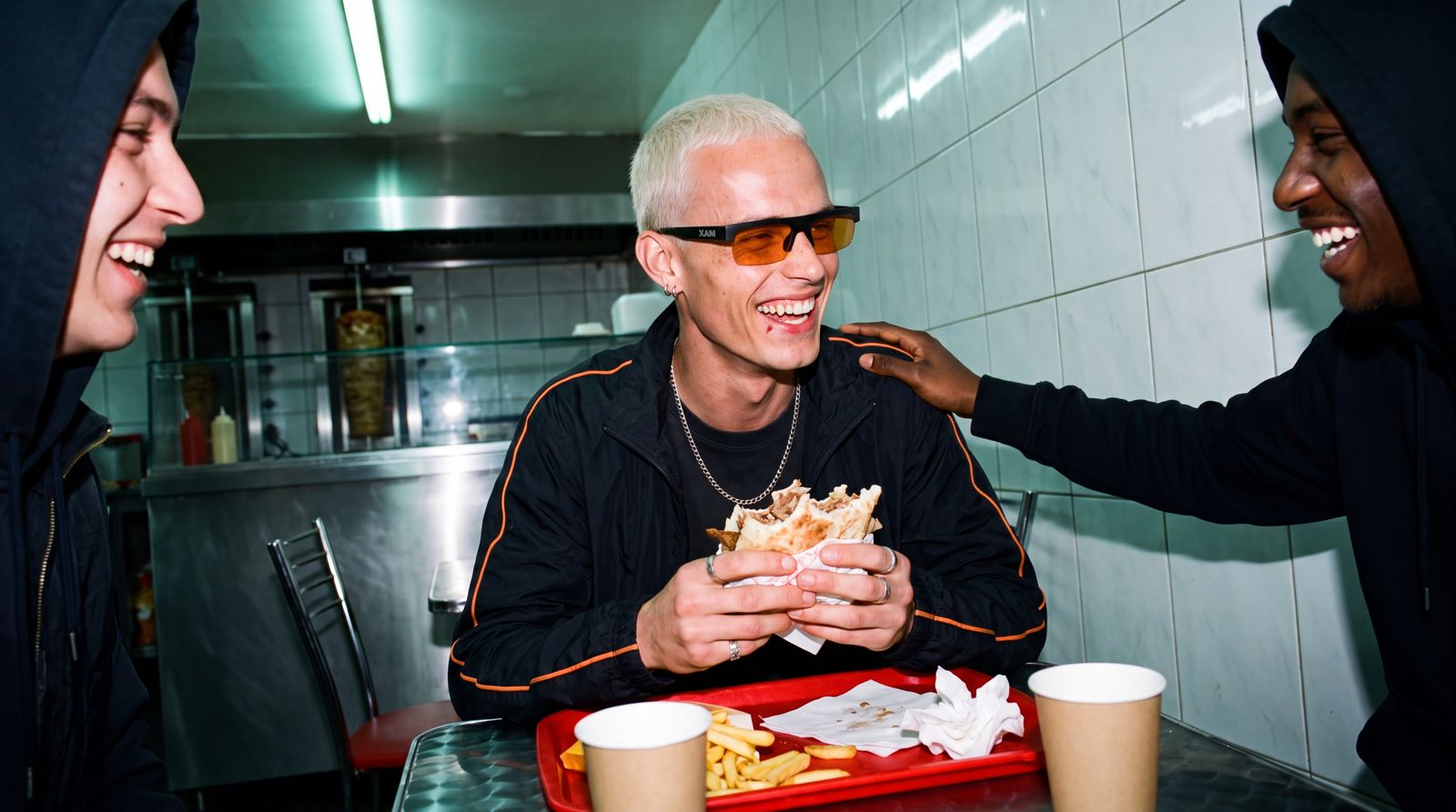 Model wearing XAM sunglasses laughing with friends in a kebab shop